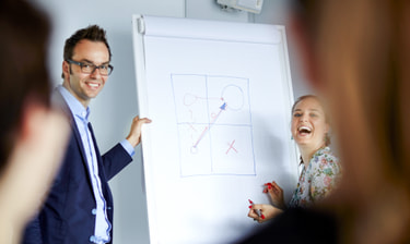 Lachende Mitarbeitende vor Flipchart Collaboratori che ridono davanti a una lavagna a fogli mobili